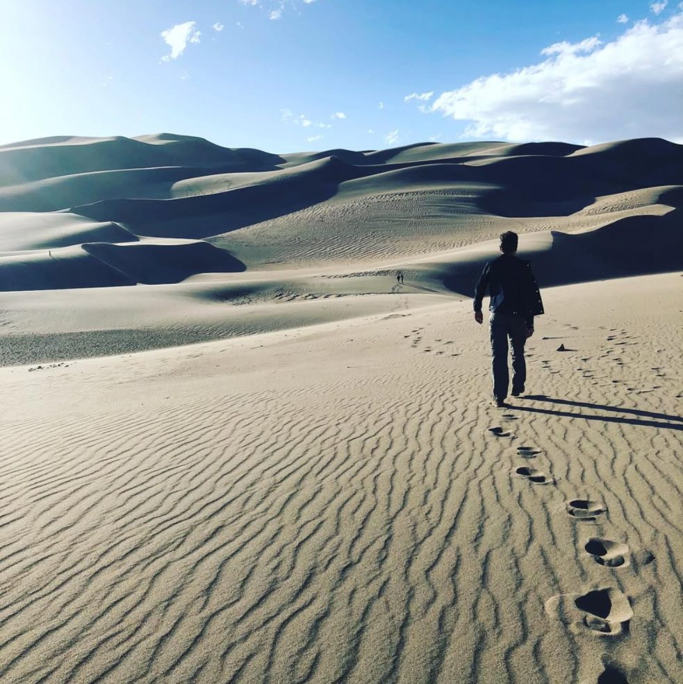Joseph, seen from behind, walking across rippled sand toward the big dunes, his footprints trailing behind him.